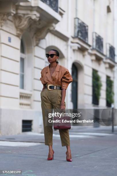 Emilie Joseph wears golden earrings, a vintage camel leather jacket worn as a top, high-waisted 7/8 paper bag pants; a black leather belt embellished...