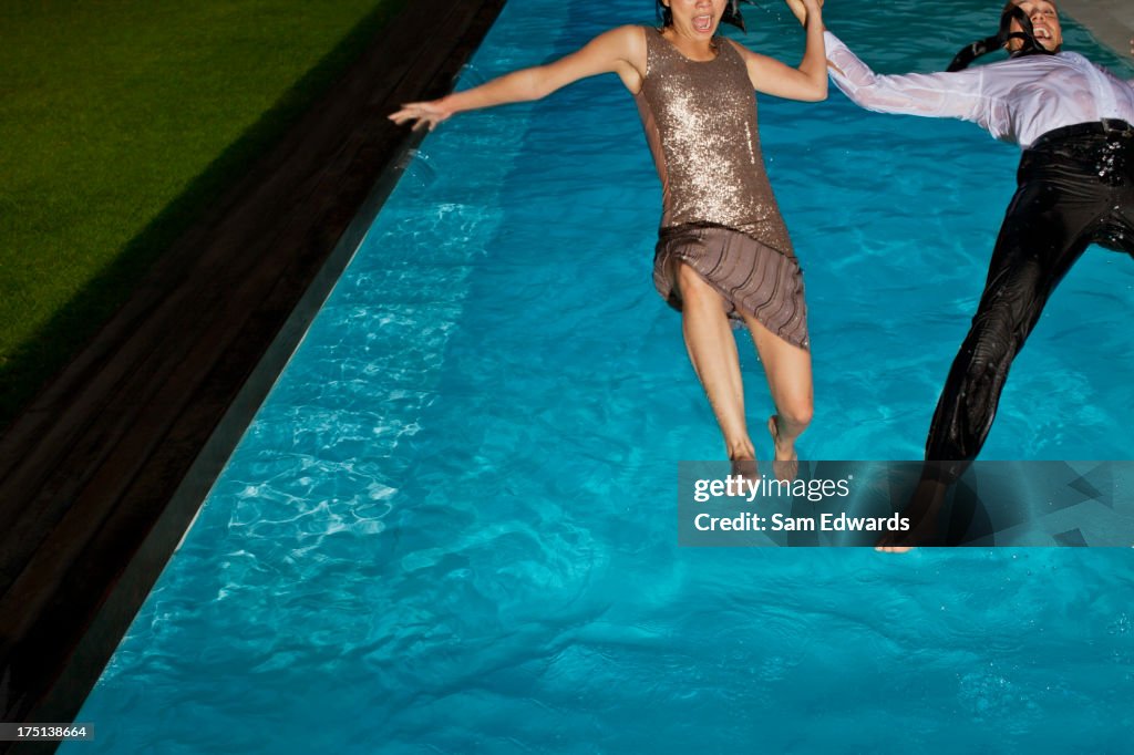 Fully dressed couple jumping into swimming pool