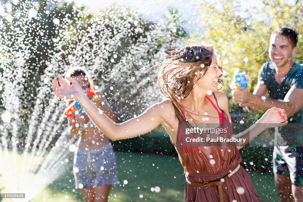 Friends playing with water guns in sprinkler