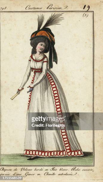 Fashionable woman with fan in huge hairstyle and hat, 1798. Velvet hat edged in white jet. Open dress decorated with chenille laces. Chapeau de...