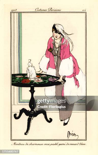 Woman in cape of pastel-pink charmeuse satin bordered with white fox fur leaning on a table. Manteau de charmeuse rose pastel garni de renard blanc....