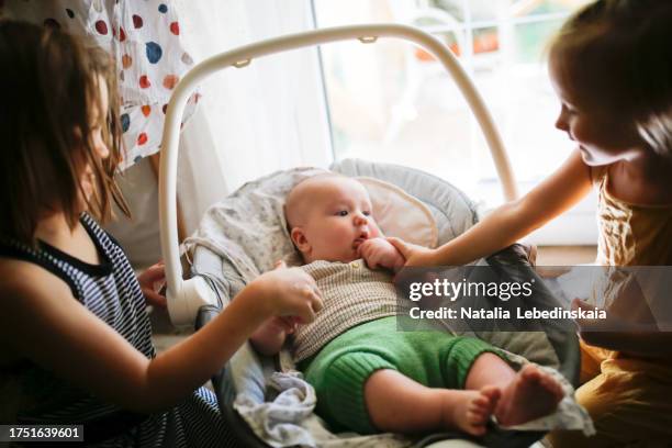 sibling love: older sisters provide tender care to chubby baby in an electric swing, dressed in a reusable diaper and woolen pants. - swinging stock pictures, royalty-free photos & images