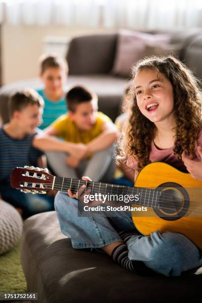 girl playing guitar while her friends talking in background - learn guitar stockfoto's en -beelden