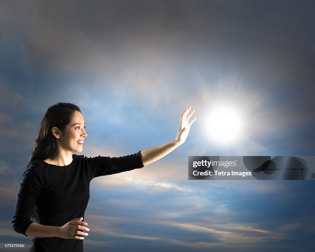 Woman reaching sun on sky, studio shot