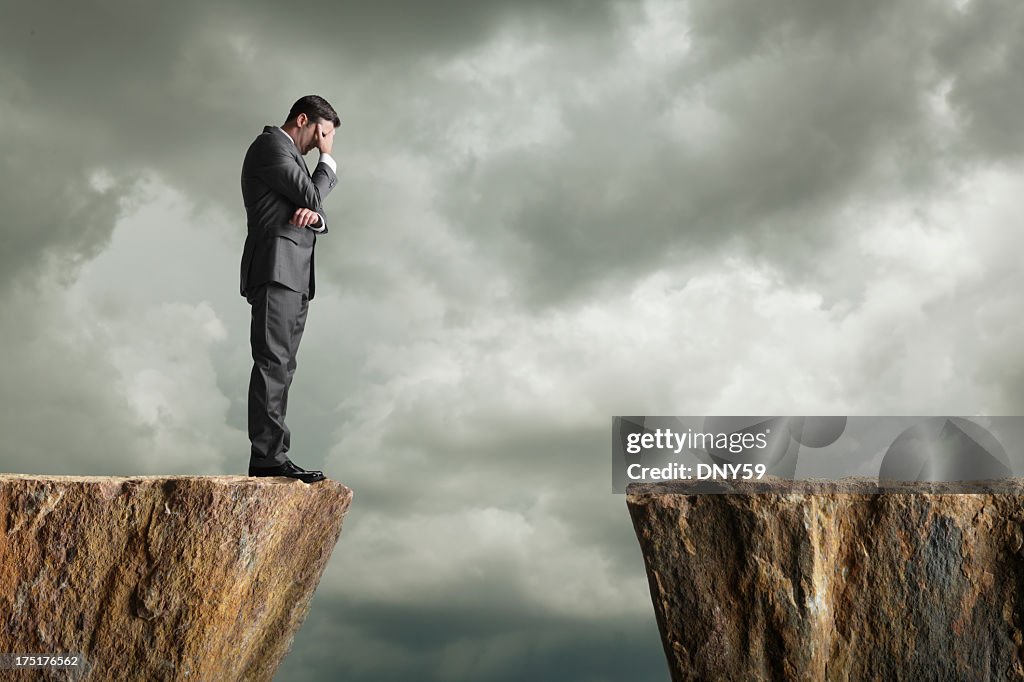 Distraught businessman standing at the edge of a cliff