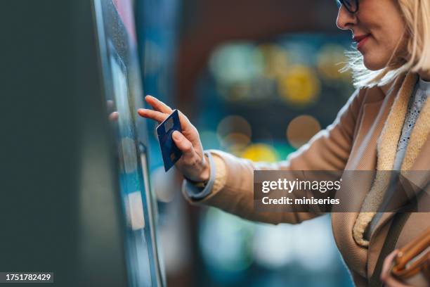 a happy beautiful blonde woman with glasses withdrawing money from atm - atm stock pictures, royalty-free photos & images