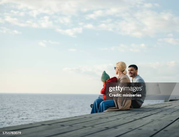 a happy beautiful family sitting near the sea while being on vacation - family stock pictures, royalty-free photos & images