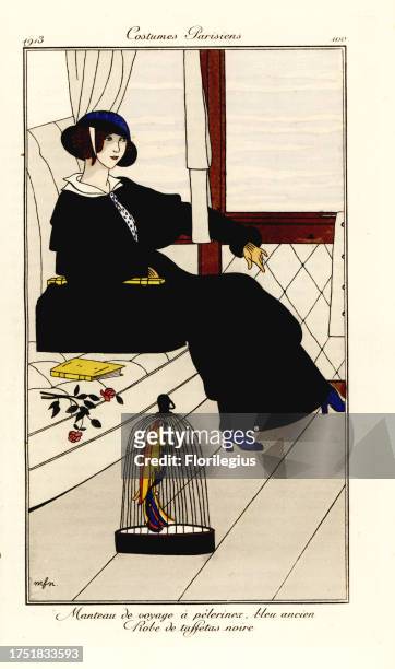 Woman in a train carriage in old-blue travel cape and black taffeta dress, with exotic bird in a cage. Manteau de voyage a pelerine, bleu ancien,...