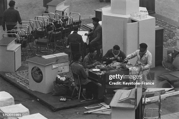 Ouvriers en pause déjeuner lors des préparatifs du salon des arts ménagers au Grand Palais à Paris, le 23 février 1955.