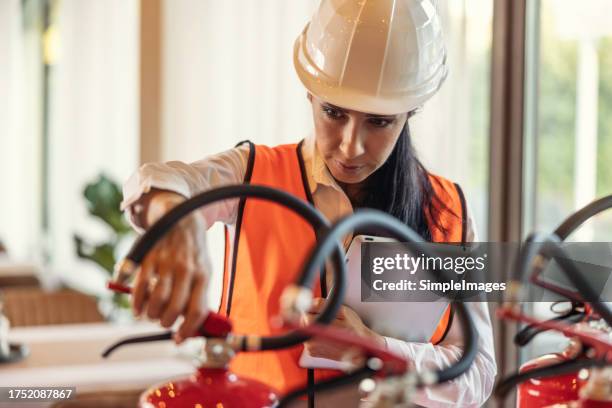 a female safety inspector checks the fire extinguishers in the hotel restaurant. - fire extinguisher inspection stock pictures, royalty-free photos & images