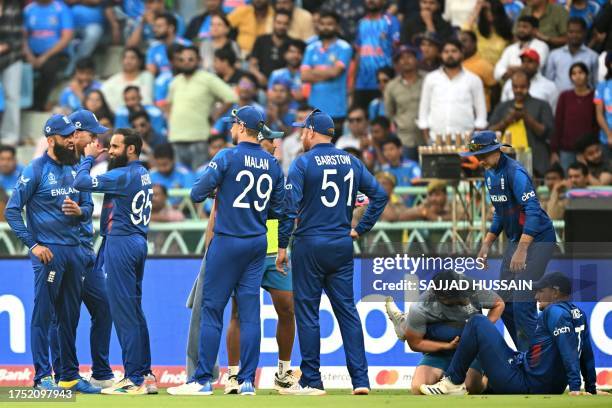 England's Liam Livingstone receives medical treatment as his teammates celebrate the dismissal of India's captain Rohit Sharma during the 2023 ICC...