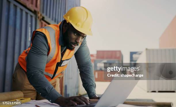 engineering man, computer and warehouse container, blueprint of floor plan at outdoor construction site. industry contractor, project manager or african person typing on laptop for safety maintenance - african creative with laptop working outside stockfoto's en -beelden