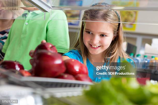 cute little girl taking apple in school lunch line - school lunch stock pictures, royalty-free photos & images