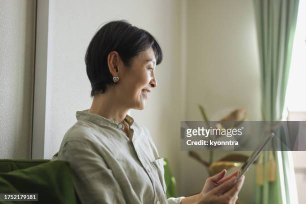 mature woman at home on tablet - alleen één oudere vrouw stockfoto's en -beelden