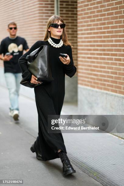 Guest wears sunglasses, pearl necklaces, a black hi-neck knit maxi dress, a large black bag, black leather army boots , outside Fendi, during the...