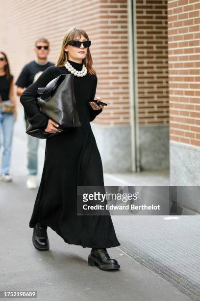 Guest wears sunglasses, pearl necklaces, a black hi-neck knit maxi dress, a large black bag, black leather army boots , outside Fendi, during the...