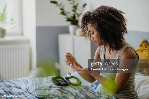 teenage girl testing her blood sample on blood sugar meter at home. - diabète photos et images de collection