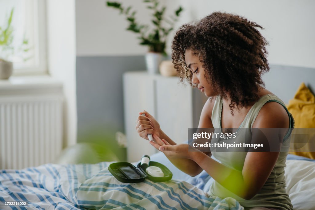 Teenage girl testing her blood sample on blood sugar meter at home.