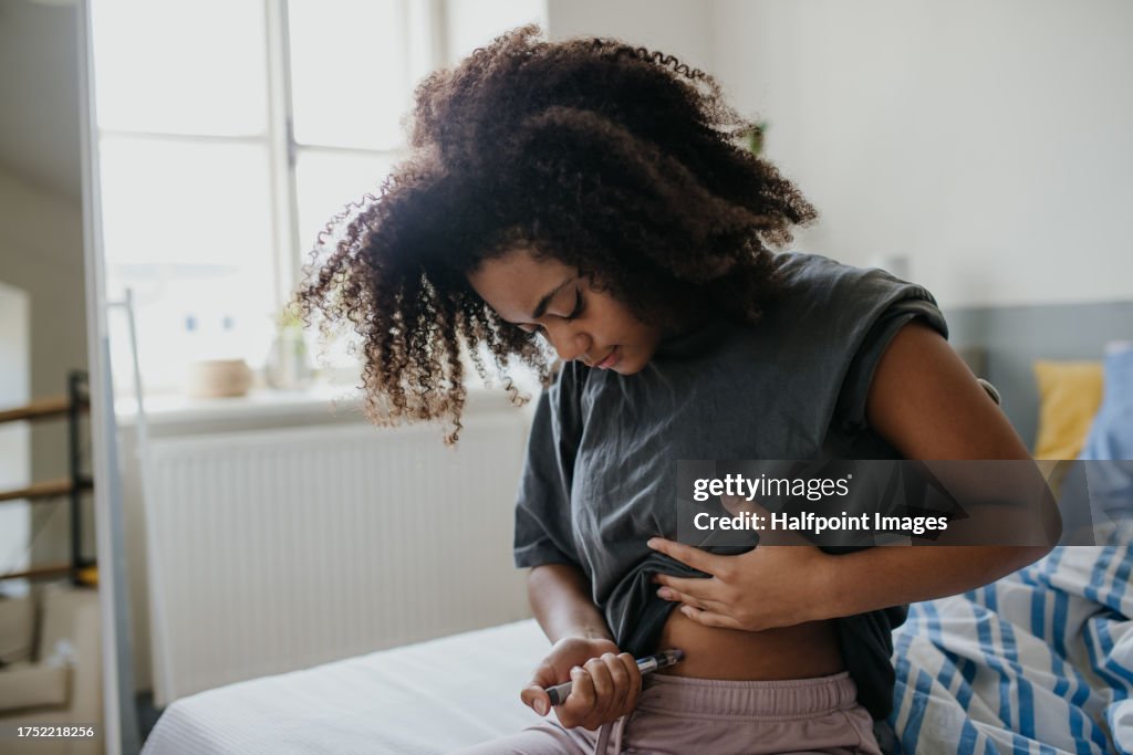 Teenage girl injecting insulin in her abdomen in the morning, feeling her blood sugar is high.