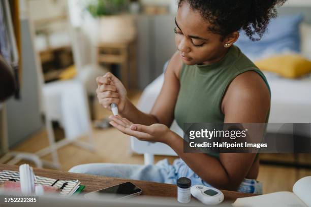 teenage girl collecting blood sample from finger for blood sugar testing at home during day. - glycemia fotografías e imágenes de stock