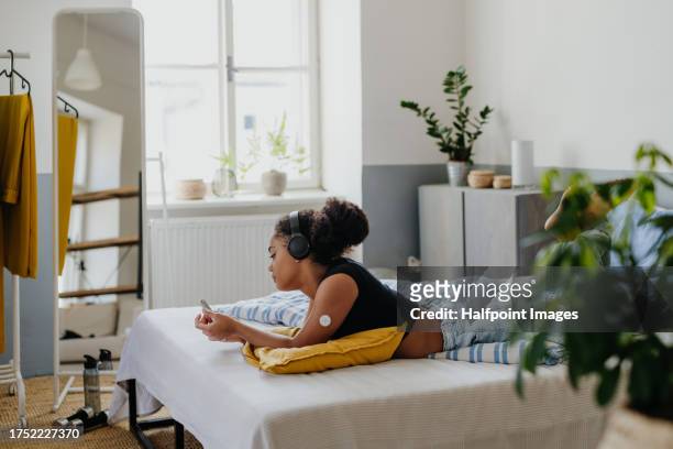 sad teenage diabetic with insulin pump, lying on bed and scrolling on smartphone, feeling lonely and depressed. teenage girl feeling different from friends, have body image issues because of insulin pump and cgm. - glucose stock pictures, royalty-free photos & images
