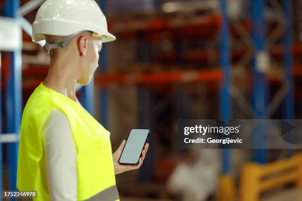 caucasian female warehouse worker is using smartphone - phone screen protector stock pictures, royalty-free photos & images