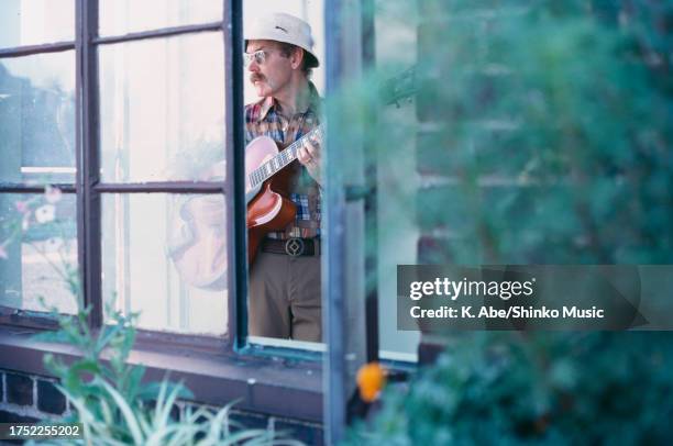 View, through a window, of American Jazz musician Jim Hall as he plays a guitar in his apartment, New York, July 1976.