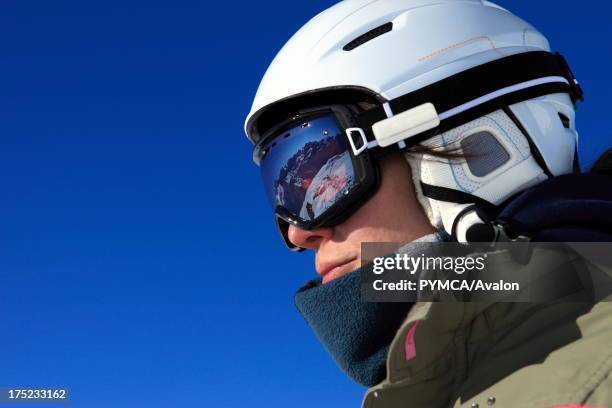 Snowboarder looks down at the valley an mountain ranges beyond, which are reflected in her goggles, Espace Killy, Tignes, FRANCE. .