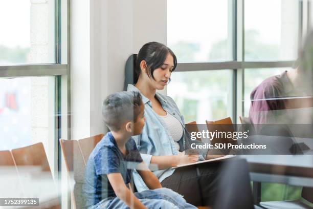 young mother fills out forms for her son to be seen by the doctor - preencher um formulário imagens e fotografias de stock