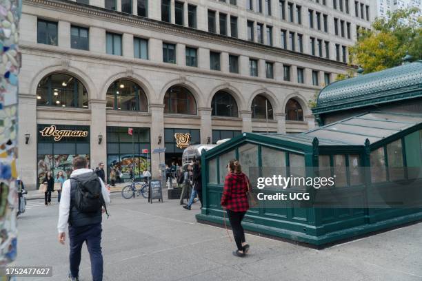 Window and the entrance to Wegmans Astor Place store is framed by a colorful art pole, partially seen on left, created by Mosaic Man, also known as...