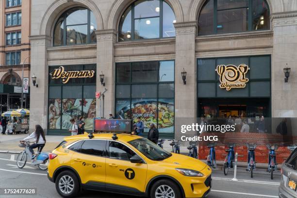 View of Wegmans Astor Place store facade and entrance shows windows displaying giant advertising banners and Now Open signs, New York, New York. This...