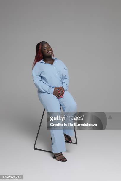 stylish young black woman with dyed hair in light blue athleisure sports suit comfortably sitting on high chair - full suit ストックフォトと画像