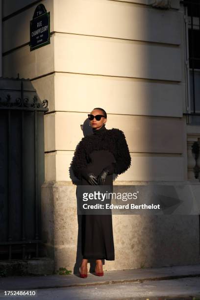 Emilie Joseph wears sunglasses, earrings, a shoulder turtleneck merino black wool maxi dress by COS in siren shape and long sleeves, paired with a...