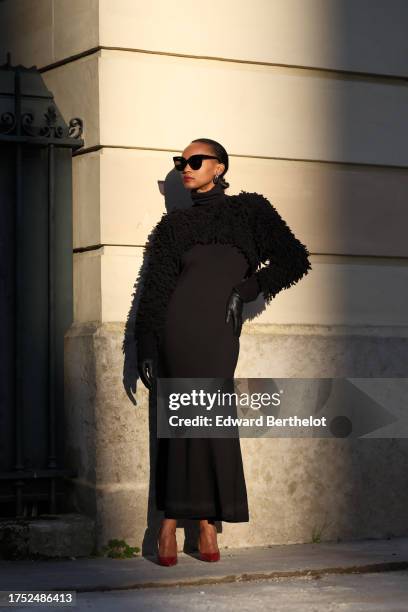 Emilie Joseph wears sunglasses, earrings, a shoulder turtleneck merino black wool maxi dress by COS in siren shape and long sleeves, paired with a...