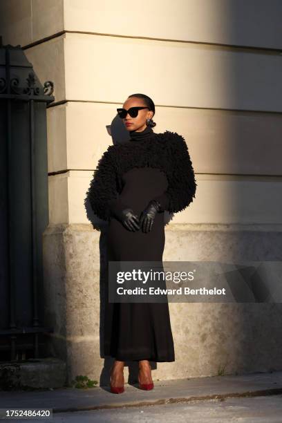 Emilie Joseph wears sunglasses, earrings, a shoulder turtleneck merino black wool maxi dress by COS in siren shape and long sleeves, paired with a...