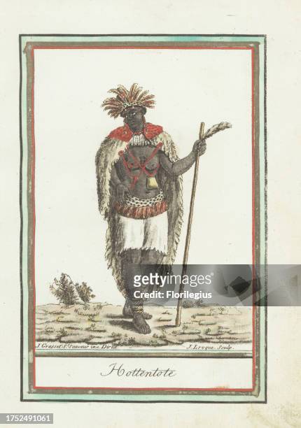 Khoikhoi woman of South Africa wearing a feather headdress, animal-skin cape, dakka or talisman hanging from a cord, loincloth, holding a staff....