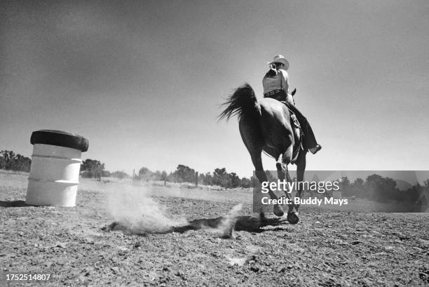 Young copwgirl practices running the barrels on her quarter horse in a dusty paddock near Santa Fe, New Mexico, 1974. .