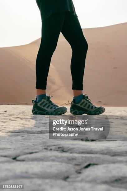 a woman wearing walking shoes walking on dead vlei basin - namibian cultures stock pictures, royalty-free photos & images