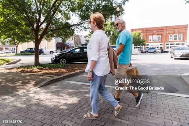 side view of senior couple crossing street together in city - couple crossing street stock pictures, royalty-free photos & images