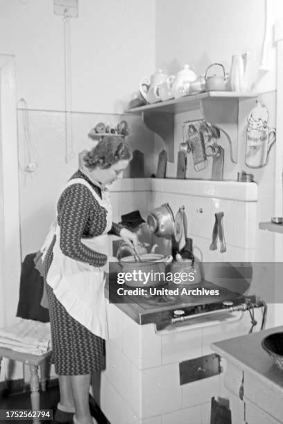 Woman standing in the kitchen on the oven cooking, Germany 1930s.