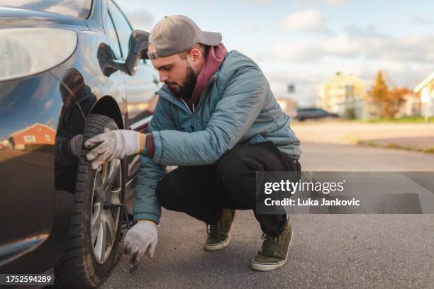 young man changing tires on his car on the roadside outdoors - car jack stock pictures, royalty-free photos & images