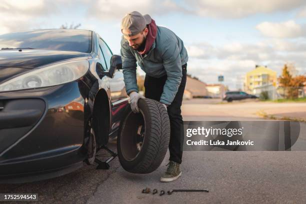 young man changing tires on his car on the roadside outdoors - spare tyre stock pictures, royalty-free photos & images