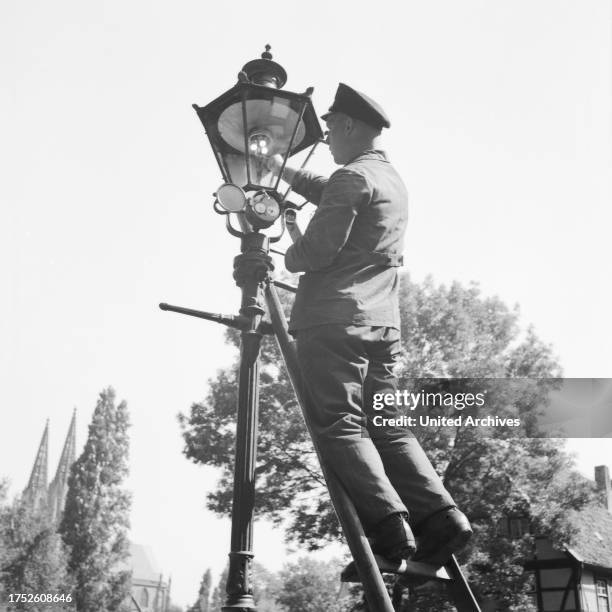 Public servant changing broken bulbs from a street lantern, Germany 1930s.