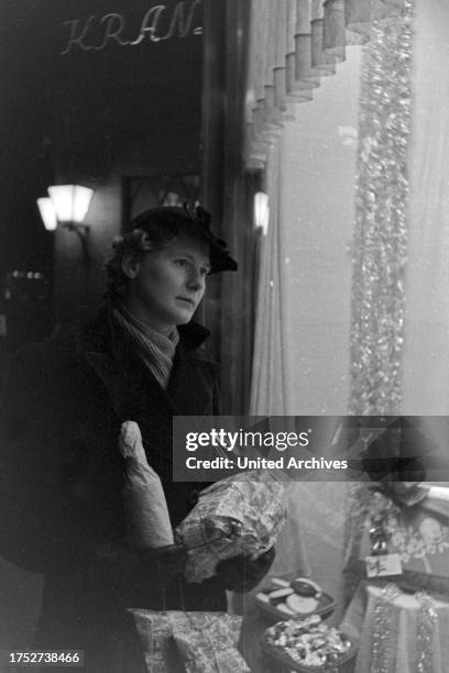 Woman watching a shop window while doing her christmas shopping near Cafe Kranzler at Berlin, Germany 1930s.