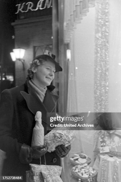 Woman watching a shop window while doing her christmas shopping near Cafe Kranzler at Berlin, Germany 1930s.