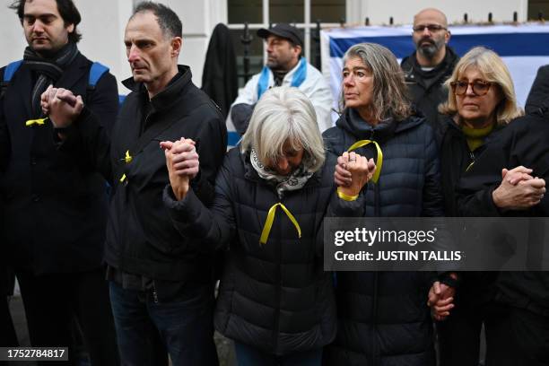 People wearing yellow ribbons hold hands as they gather outside the Qatari Embassy in London on October 29 to demand the release of the estimated 230...