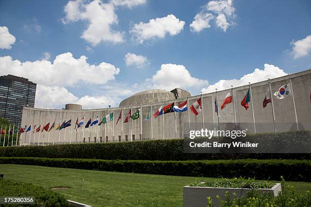 flags and concrete building above grass and shrubs - edificio de las naciones unidas fotografías e imágenes de stock