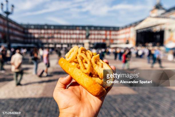 man eating bocadillo de calamares (calamari sandwich) on plaza mayor, madrid, spain - meal fotografías e imágenes de stock