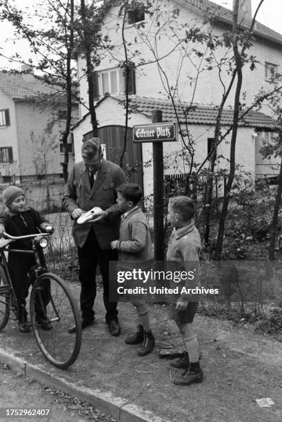 The mayor of Zeppelinheim and airship captain Hans von Schiller winding up the toy car of three boys on the street, near Frankfurt am Main, Germany...