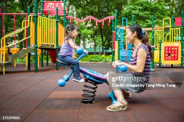 toddler girl playing seesaw with young mom - área de juego fotografías e imágenes de stock